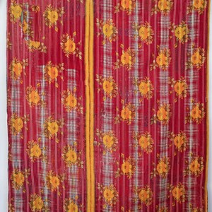 Könnte beinhalten: Ein roter Stoff mit gelbem Blumenmuster. Das Design umfasst vertikale Streifen und einen zentralen gelben Streifen. Gelbe Blumenmotive sind auf dem roten Hintergrund verteilt. Es handelt sich wahrscheinlich um eine Decke oder einen Überwurf.