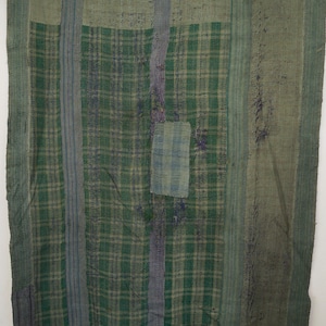 May include: A patchwork quilt in shades of green and blue, featuring a plaid design. The rectangular quilt is constructed from various fabric pieces stitched together. The colour scheme includes green, blue, and grey tones.