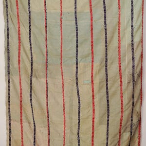 Op de afbeelding: Een rechthoekig textiel met een lichtcrème basis en verticale strepen in afwisselend rood en donkerblauw. De strepen zijn versierd met geometrische patronen. Een horizontale rand met een rood en blauw patroon omlijst de boven- en onderkant.