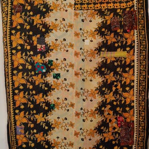 Könnte beinhalten: Eine dekorative Steppdecke mit einem Blumenmuster in Schwarz, Creme und Gold. Die Steppdecke hat ein sich wiederholendes Blumendesign und Patchwork-Quadrate. Die Ränder sind mit einem detaillierten Rand versehen.