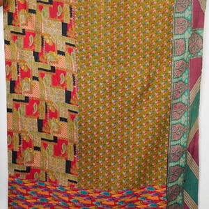 Op de afbeelding: Een rechthoekig textiel met een patchworkontwerp bestaande uit meerdere panelen. Eén sectie toont een rood en zwart raster met paisley-motieven, een andere een groen bloemenpatroon en een derde een rode basis met kleurrijke abstracte vormen.