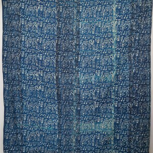 Puede incluir: Un textil rectangular grande con un fondo azul oscuro y un patrón repetido de símbolos blancos estilizados. La tela parece estar drapeada, con pliegues y arrugas visibles. El diseño general sugiere un tema cultural o artístico.
