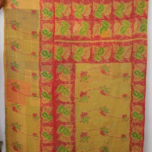 Op de afbeelding: Een rechthoekig textiel met een patchworkontwerp met secties van gele en mosterdkleurige stof. De stof is versierd met herhalende patronen van groene bladeren en rode bloemenranken, gescheiden door verticale rode randen met bladmotieven.
