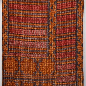 May include: A rectangular textile featuring a patchwork design with alternating panels of deep red, burnt orange, and dark charcoal grey. The fabric displays a grid-like pattern with repeating floral motifs and horizontal stripes throughout the surface.