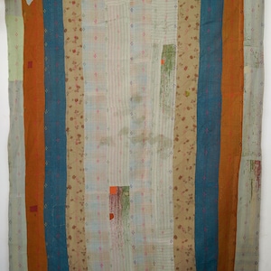 May include: A patchwork quilt with vertical stripes in shades of teal, orange, and beige. The quilt incorporates floral and geometric patterns, with visible stitching. The design is a blend of textures and colours, creating a unique textile.