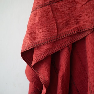 Puede incluir: Primer plano de una tela roja texturizada con un diseño en capas. La tela tiene un patrón ondulado y está acentuada con costuras oscuras a lo largo de los bordes y las costuras. Los pliegues crean una sensación de profundidad y textura.