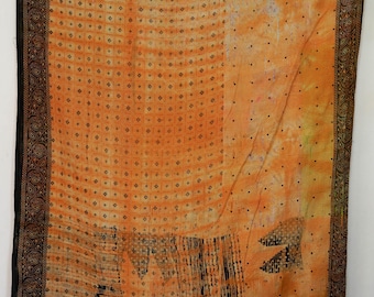 Könnte beinhalten: Ein orangefarbenes Textil mit einem sich wiederholenden quadratischen Muster und verstreuten schwarzen Punkten. Die Ränder sind mit einem schwarzen und braunen Paisley-Design eingefasst. Das Textil hat ein verblasstes, Vintage-Aussehen.