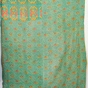 Puede incluir: Textil verde con un patrón intrincado. La sección superior presenta paneles rectangulares con un diseño repetitivo en naranja y amarillo. El cuerpo principal tiene un patrón floral repetitivo en naranja y amarillo. Los bordes están ribeteados con un borde verde oscuro.