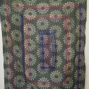 Op de afbeelding: Donkergroen textiel met een herhalend cirkelvormig patroon in roze, blauw en geel. Het ontwerp omvat een centraal vierkant en verticale strepen, waardoor een gelaagd effect ontstaat. De stof lijkt lichtgewicht, ideaal voor een sprei of decoratief stuk.