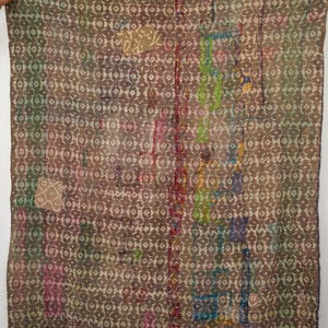 May include: A brown and beige patterned textile with a repeating geometric design. Patches of various colours, including red, green, and blue, are sewn onto the fabric. The textile appears to be a quilt or blanket.