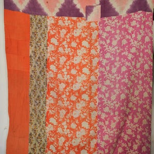 Może przedstawiać: Pikowana narzuta patchwork z różnymi wzorami i kolorami. Górna część ma wzór rombów w kolorze różowym i fioletowym. Poniżej znajdują się pionowe paski z pomarańczowych, kwiatowych i różowych tkanin. Narzuta jest wykonana z miękkiej tkaniny.