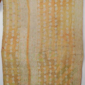 May include: A rectangular textile featuring a yellow and orange colour palette with vertical stripes and a repeating pattern of small white leaf motifs. The fabric displays visible stitching throughout, creating a textured appearance across the surface.