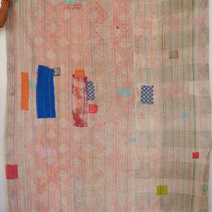 May include: A rectangular textile quilt featuring a patchwork design with a light pink and beige base. The fabric is adorned with vertical stripes, subtle diamond patterns, and various small, colorful rectangular patches in blue, orange, and red.