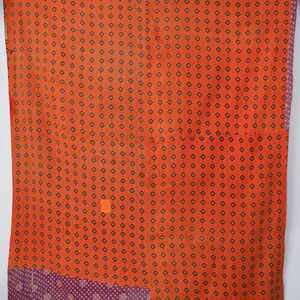May include: A rectangular textile featuring a vibrant orange base with a repeating pattern of small black and white diamond shapes. The fabric includes a contrasting purple section at the bottom with a white dotted pattern and visible stitching.