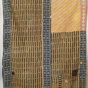 Puede incluir: Un edredón de retazos con una mezcla de patrones y colores. El edredón presenta rayas verticales en amarillo y gris, con una sección de líneas diagonales amarillas y blancas. Los bordes tienen un borde de pequeños cuadrados y círculos.