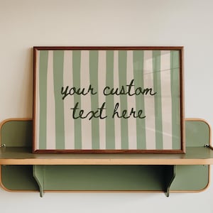 Peut inclure: Une affiche encadrée avec un motif à rayures vertes et blanches et le texte "your custom text here". L'affiche est exposée sur une étagère verte et beige, fixée à un mur blanc. L'étagère a un design arrondi.