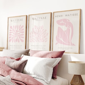 May include: Three framed art prints featuring pink abstract designs. The prints are hung on a white wall above a bed with pink bedding.