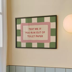Puede incluir: Un estampado enmarcado con el texto "TEXT ME IF YOU RUN OUT OF TOILET PAPER". El estampado tiene un borde rosa y un fondo a cuadros verdes y blancos. El marco es negro.