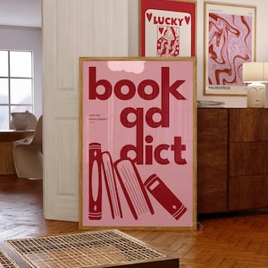 Peut inclure: Une affiche rose et rouge avec le texte "book addict" en grandes lettres rouges. Le texte "Just one more chapter" est en lettres rouges plus petites sous le texte principal. Il y a cinq livres rouges empilés les uns sur les autres dans le coin inférieur gauche de l'affiche.