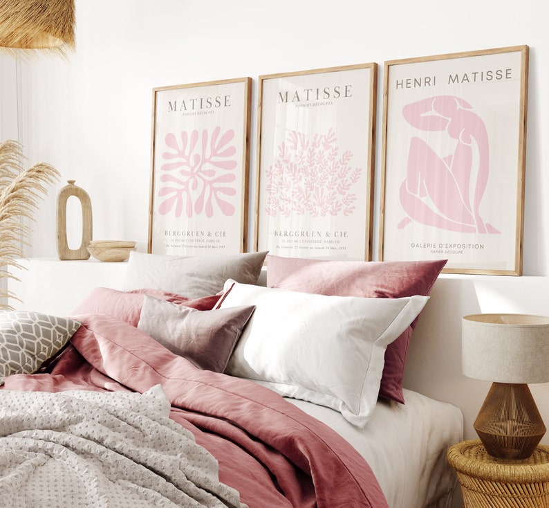 May include: Three framed art prints featuring pink abstract designs. The prints are hung on a white wall above a bed with pink bedding.