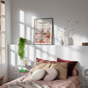 May include: A bedroom with a bed with a pink duvet and a white and brown pillow. There is a framed poster on the wall that says "PAUL KLEE" and a plant on a side table.