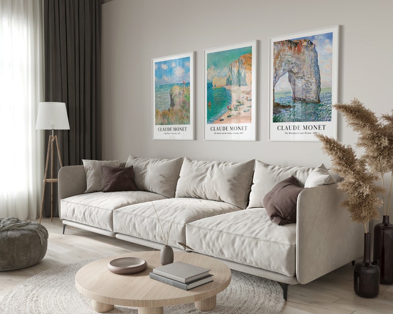 May include: Three framed art prints of seascapes by Claude Monet. The prints are hung on a light beige wall above a white couch. The prints are all in white frames with a white mat.