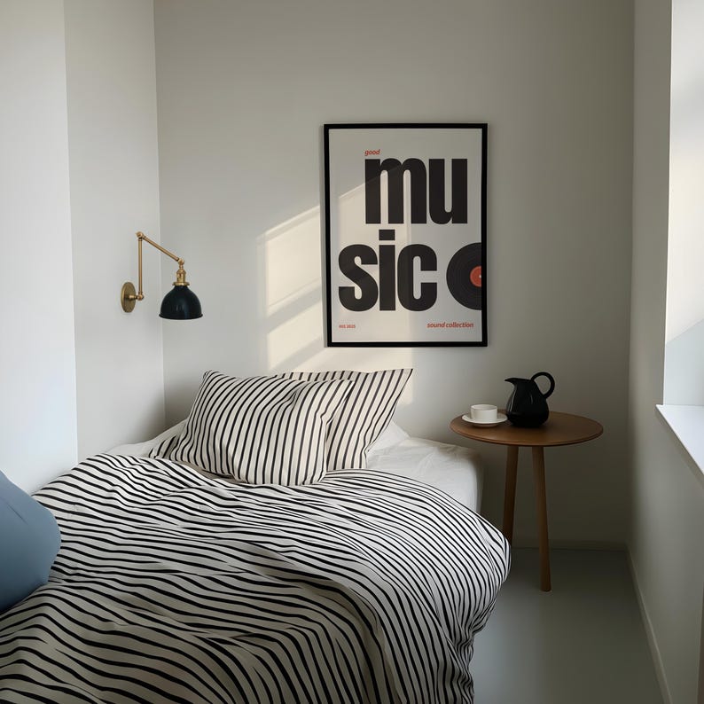 May include: A bedroom scene featuring a bed with black and white striped bedding and pillows. A framed poster with the word "music" in large black letters hangs on the wall. A small wooden side table holds a black pitcher and a white teacup.