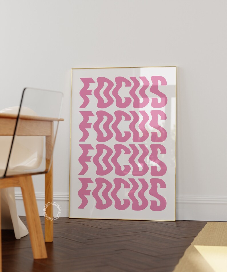 May include: A framed print with the word "FOCUS" repeated four times in a pink, wavy font on a white background. The frame is gold.