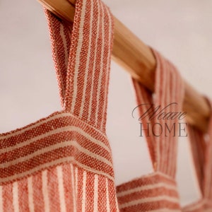 May include: Close-up of red and white striped fabric curtain panels with a wooden rod. The fabric has a woven texture and is hanging in soft folds.
