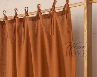 May include: A set of rust-colored curtains with a simple tie-top design. The curtains are hanging from a wooden rod.