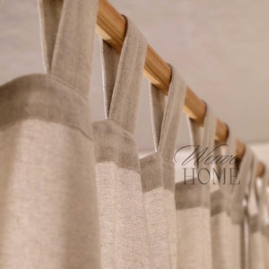 May include: Close-up of a set of beige linen curtains with a wooden rod. The curtains have a simple design with a loop at the top for hanging.