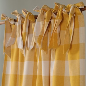 May include: Yellow and white checked curtains with tie-top fastenings. The curtains are suspended from a wooden rod. The fabric features a classic gingham pattern, and the tie-tops are a solid yellow colour.