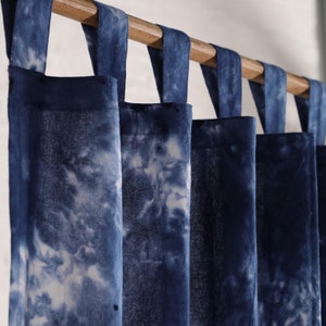 Op de afbeelding: Blauwe tie-dye gordijnen met witte accenten die aan een houten roede hangen.