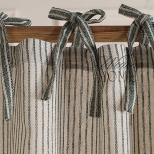 May include: Three green and white striped fabric curtains with green ribbon ties hanging from a wooden rod.