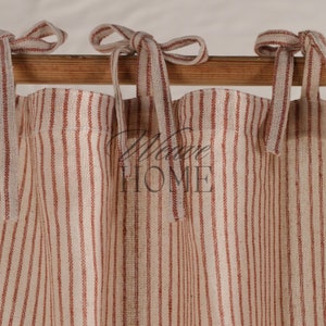 May include: A pair of cream-colored curtains with thin red stripes, tied back with matching fabric ties. The curtains are hung on a wooden rod.