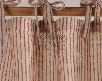 May include: A pair of cream-colored curtains with thin red stripes, tied back with matching fabric ties. The curtains are hung on a wooden rod.