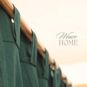 Puede incluir: Primer plano de un conjunto de cortinas verde oscuro colgadas de una barra de madera. Las cortinas están hechas de una tela suave y texturizada. El texto "Weave HOME" es visible en el fondo.