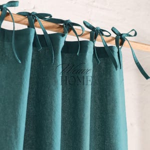 Puede incluir: Cortinas de lino color turquesa con una barra de madera y atadas con lazos de tela a juego. Las cortinas están colgadas en una ventana y el texto "Weave Home" es visible en el centro de la imagen.