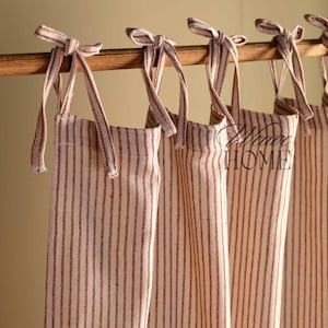 May include: Four red and white striped fabric curtains with ties hanging on a wooden rod. The curtains are tied back with fabric ties.
