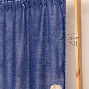 Op de afbeelding: Een blauw fluwelen gordijnpaneel met een roedezak aan de bovenkant, met een zachte, lichtreflecterende textuur. De stof heeft een diepblauwe kleur en bevat de tekst Weave HOME in een donker lettertype aan de rechterkant van het gordijn.