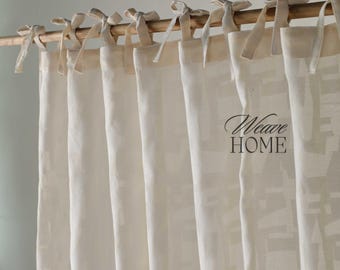 Peut inclure: Rideaux en lin blanc cassé suspendus à une tringle en bois, attachés avec des nœuds en tissu assortis. Les rideaux présentent un motif géométrique subtil et le texte "Weave HOME" est visible.