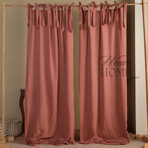 Puede incluir: Dos cortinas de color coral con rayas verticales y cierres superiores con lazos. Las cortinas cuelgan de una barra de madera. El texto "Wave HOME" está impreso en la cortina derecha.