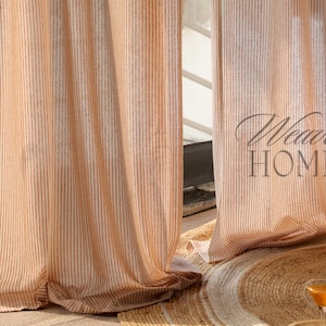 Op de afbeelding: Een paar transparante, gestreepte gordijnen in een lichtbruine en witte kleurstelling. De gordijnen hangen in een raam en zijn gedeeltelijk dichtgetrokken. De tekst "Weave Home" is zichtbaar in de rechterbenedenhoek van de afbeelding.