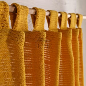Può includere: Cinque tende a crochet gialle con una trama tessuta sono appese a un'asta di legno. Le tende hanno un anello in cima per l'appeso.