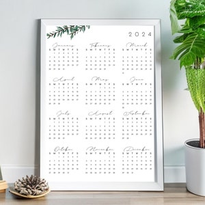 Peut inclure: Un calendrier blanc encadré avec un motif floral en haut. Le calendrier est pour l'année 2024 et comprend les 12 mois.