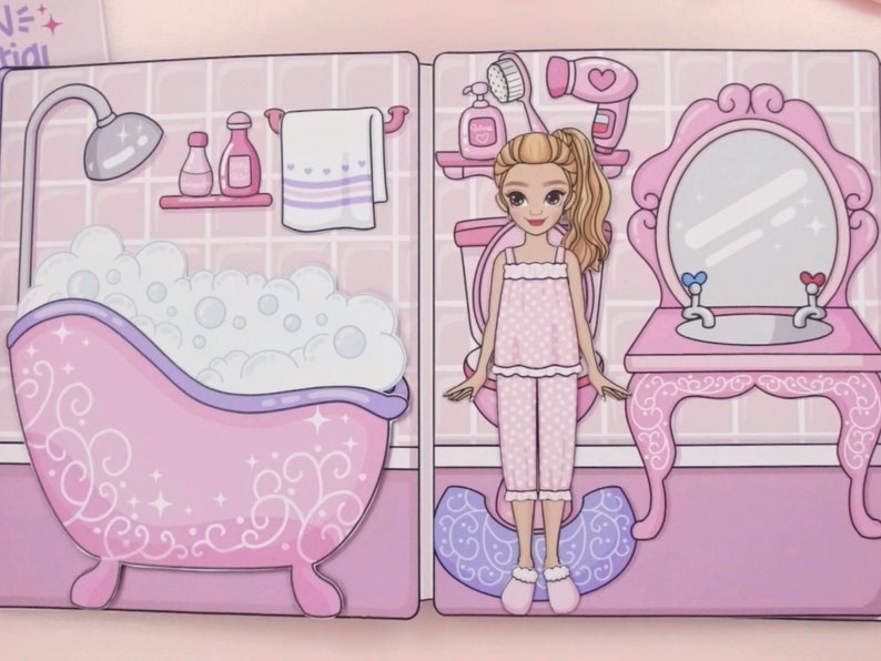 Op de afbeelding: Een papieren poppensc&egrave;ne met een badkamer met een roze badkuip vol bubbels, een douche en een wastafel. De pop draagt een roze pyjama en staat voor een toilet en een spiegel. De sc&egrave;ne is gedecoreerd in roze tinten.