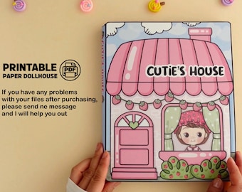 May include: Printable paper dollhouse of a pink and white house with a strawberry theme. The house has a sign that says "Cutie's House".