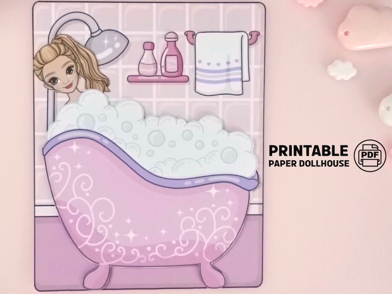 Op de afbeelding: Een afdrukbare papieren poppenhuis sc&egrave;ne met een cartoonvrouw in een badkuip vol bubbels. De roze badkuip heeft decoratieve krullen. De sc&egrave;ne bevat een douchekop, toiletartikelen en een handdoek. De tekst "PRINTABLE PAPER DOLLHOUSE" is zichtbaar.