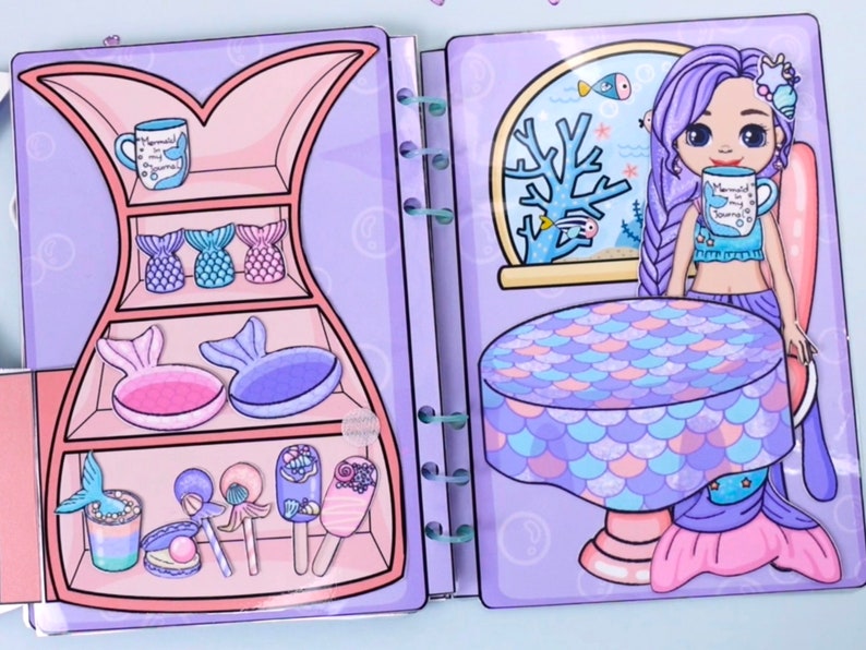 May include: A paper doll playset featuring a mermaid theme. The set includes a mermaid character with purple hair, a table, and various accessories like mermaid tails, mugs, and lollipops. The color palette is primarily pastel purples, pinks, and blues.