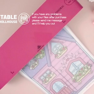 Op de afbeelding: Een printbaar papieren poppenhuisontwerp met een roze omslag en de tekst "PRINTABLE PAPER DOLLHOUSE". De illustratie van het poppenhuis toont een roze huis met bloembakken en een hartvormig wijnstokontwerp. De tekst "If you have any problems..." is ook zichtbaar.